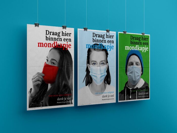 Drie posters met de tekst 'Draag hier binnen een mondkapje' hangen aan de muur. Op elke poster een persoon met een mondkapje.