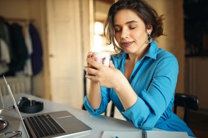 Vrouw met kop koffie in haar handen luistert naar een laptop doe het scherm aan haar voorleest